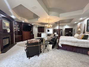 Bedroom with a tray ceiling, visible vents, a chandelier, carpet floors, and a premium fireplace