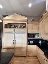 Kitchen with light wood finished floors, open shelves, light brown cabinets, and built in microwave