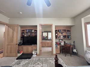 Bedroom featuring built in desk, light carpet, ensuite bathroom, and ceiling fan