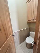 Bathroom featuring toilet, tile walls, tile patterned floors, and a wainscoted wall