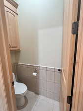 Bathroom featuring a wainscoted wall, toilet, tile walls, and tile patterned floors