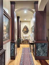 Corridor featuring arched walkways, baseboards, light wood-style flooring, and recessed lighting