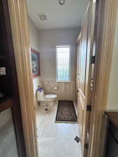 Half bath with tile walls, toilet, visible vents, tile patterned floors, and a wainscoted wall