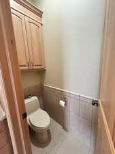 Bathroom with wainscoting, tile patterned flooring, tile walls, and toilet