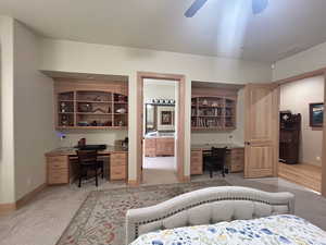 Bedroom with a ceiling fan, baseboards, ensuite bathroom, light carpet, and built in desk