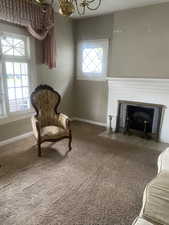 Living area featuring a notable chandelier, a brick fireplace, baseboards, and carpet