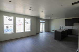 Kitchen featuring dark cabinetry, a center island with sink, open floor plan, and wood finished floors