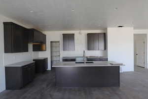 Kitchen featuring a sink, a center island with sink, light countertops, tasteful backsplash, and dark wood-style floors