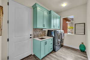 Laundry area featuring cabinet space, a sink, baseboards, light wood finished floors, and washer and clothes dryer