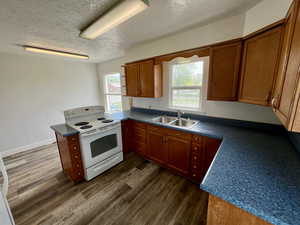 Kitchen with a sink, white electric stove, dark countertops, a textured ceiling, and dark wood-type flooring