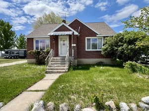 View of front of property featuring a shingled roof, brick siding, a chimney, and a front yard