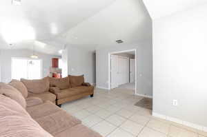 Living room featuring light tile patterned flooring, vaulted ceiling, baseboards, and visible vents
