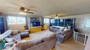 Living room featuring ceiling fan, light carpet, and a textured ceiling