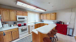 Kitchen with a sink, white appliances, light countertops, and a center island