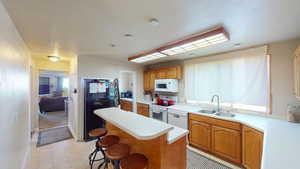 Kitchen featuring a breakfast bar area, a center island, a sink, white appliances, and light countertops
