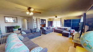Living room featuring carpet flooring, a textured ceiling, a brick fireplace, and ceiling fan