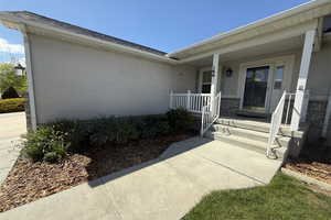 View of exterior entry with covered porch, roof with shingles, and stucco siding
