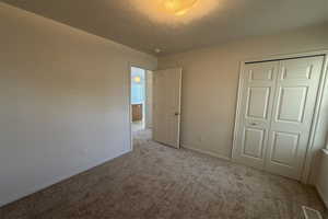Unfurnished bedroom with carpet flooring, a closet, a textured ceiling, and baseboards