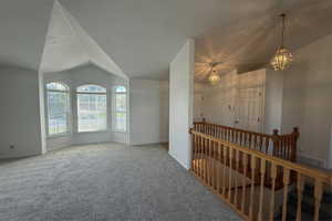 Carpeted empty room featuring baseboards, lofted ceiling, and a notable chandelier