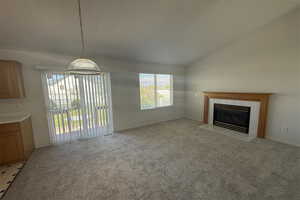 Unfurnished living room with vaulted ceiling, light carpet, baseboards, and a tile fireplace