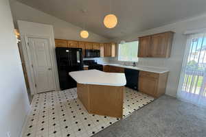 Kitchen with vaulted ceiling, a sink, black appliances, decorative light fixtures, and a kitchen island