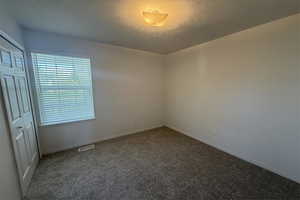 Spare room featuring a textured ceiling, carpet flooring, baseboards, and visible vents