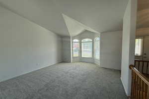 Carpeted spare room featuring baseboards, visible vents, and vaulted ceiling