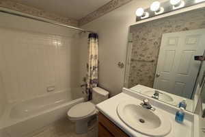Full bathroom with vanity, shower / bathtub combination with curtain, and toilet