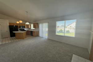 Kitchen featuring lofted ceiling, open floor plan, a kitchen island, black appliances, and light countertops