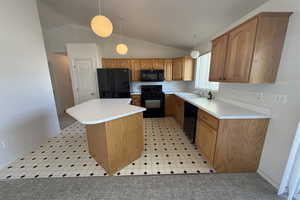 Kitchen with a sink, black appliances, light countertops, a kitchen island, and lofted ceiling