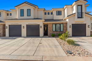 Multi unit property with an attached garage, stucco siding, brick siding, and driveway
