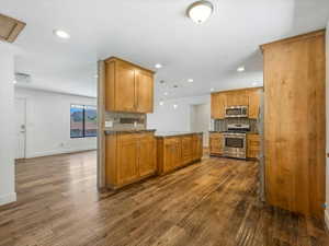 Kitchen with stainless steel appliances, dark wood-type flooring, recessed lighting, decorative backsplash, and baseboards