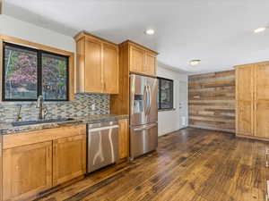 Kitchen with a sink, dark stone countertops, dark wood-type flooring, backsplash, and appliances with stainless steel finishes
