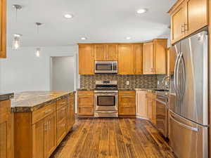 Kitchen with dark wood-style flooring, a sink, brown cabinets, stainless steel appliances, and tasteful backsplash