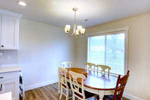Dining space with a textured ceiling, light wood-type flooring, visible vents, a chandelier, and baseboards