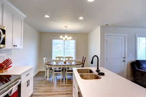 Kitchen featuring a notable chandelier, light wood-style flooring, a healthy amount of sunlight, a sink, and white cabinetry