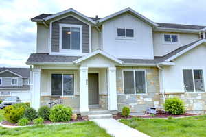View of front of home featuring a shingled roof, stucco siding, stone siding, and a front yard