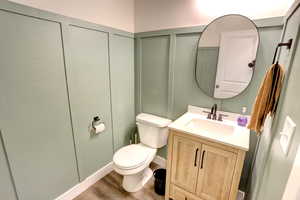 Half bathroom with vanity, toilet, a decorative wall, and wood finished floors