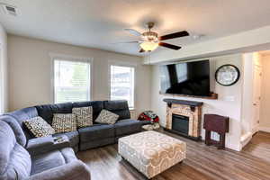 Living room with wood finished floors, a textured ceiling, visible vents, a ceiling fan, and a stone fireplace
