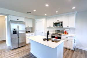 Kitchen with a sink, visible vents, light wood-style flooring, baseboards, and appliances with stainless steel finishes