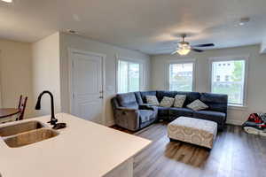 Living area featuring wood finished floors, a textured ceiling, visible vents, ceiling fan, and baseboards