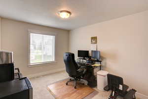 Carpeted office featuring a textured ceiling, baseboards, and visible vents