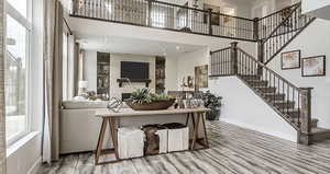 Living area with wood finished floors, plenty of natural light, stairway, baseboards, and a towering ceiling