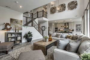 Living area with wood finished floors, a notable chandelier, visible vents, stairway, and a towering ceiling