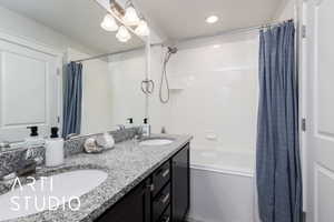 Bathroom with recessed lighting, double vanity, shower / bath combo with shower curtain, and a sink