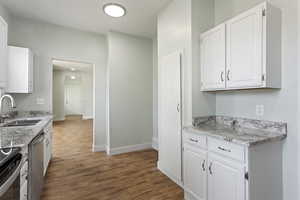 Kitchen with dark wood-style flooring, stainless steel dishwasher, a sink, baseboards, and white cabinetry