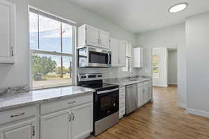 Kitchen with white cabinets, light stone countertops, appliances with stainless steel finishes, a sink, and light wood-style flooring