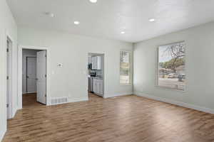 Unfurnished living room with light wood-style floors, baseboards, recessed lighting, and visible vents