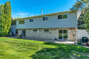 Rear view of house featuring fence, a patio, stone siding, and a lawn