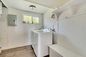 Washroom with electric panel, laundry area, dark wood-type flooring, washer and dryer, and baseboards